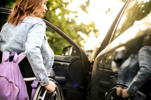 Junge Frau im Rollstuhl öffnet die Fahrertür eines Autos